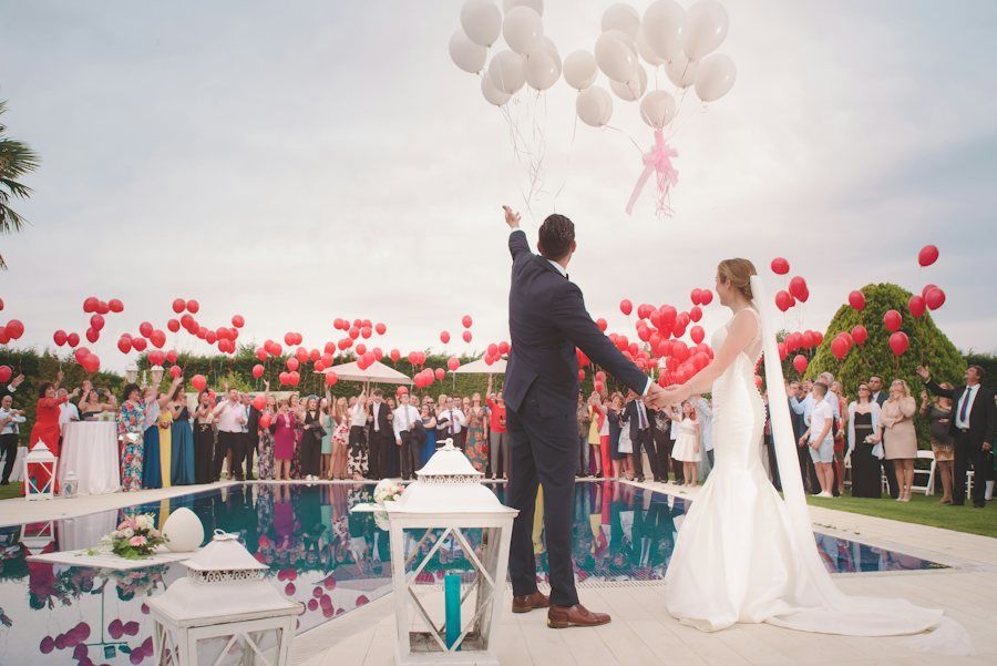 Outdoor wedding with red balloons and guests around a pool